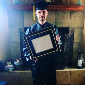 A man in a green graduation robe holding a framed diploma