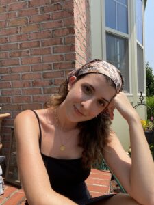 A girl with brown hair wearing a headband sitting outside in a black tank top