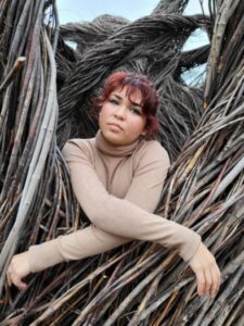 a woman with red hair wearing a Tain turtle neck posing in the center of branches